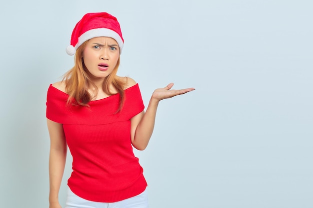 Retrato de mujer joven con vestido de Navidad mostrando algo con palmas con expresión de asombro