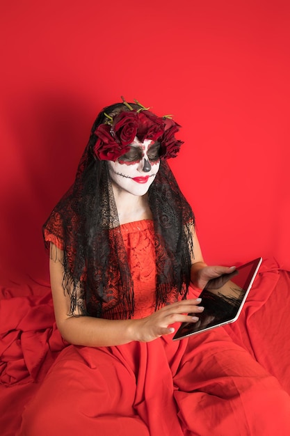 Retrato de una mujer joven con un vestido rojo y maquillaje tradicional de calaveras de azúcar para la celebración del Día de los Muertos el Día de los Muertos