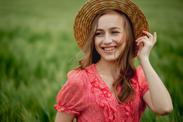 Retrato de mujer joven en vestido y sombrero en campo verde de cebada en campo. Chica elegante en rústico disfrutando momento pacífico en hierba en verano. Momento rural tranquilo