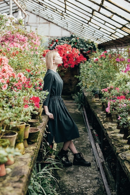 Retrato de una mujer joven con un vestido verde en un invernadero con azaleas florecientes rojas y rosadas