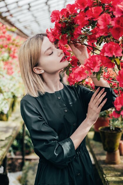 Retrato de una mujer joven con un vestido verde en un invernadero con azaleas florecientes rojas y rosadas