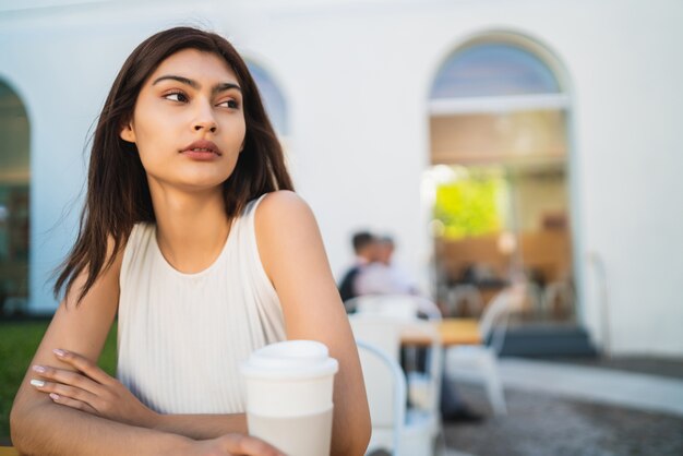 Retrato de mujer latina joven disfrutando y bebiendo una taza de café al aire libre en la cafetería. Concepto de estilo de vida.