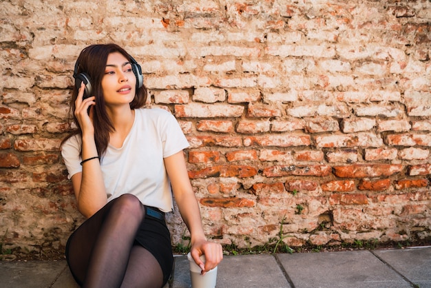 Retrato de mujer latina joven relajarse y escuchar música con auriculares contra la pared de ladrillo. Concepto urbano.