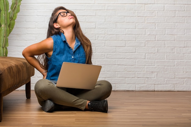 Retrato de una mujer latina joven sentada en el suelo con dolor de espalda debido al estrés laboral