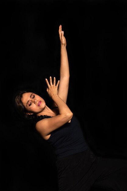 Retrato de una mujer latina posando aislada sobre fondo negro mirando hacia abajo y estirando su brazo hacia arriba Concepto de expresión corporal femenina