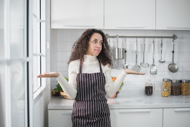 Retrato de una mujer latina sonriendo alegremente y mostrando varios gestos en la cocina.