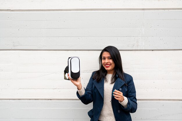 Retrato de mujer latina sonriente mirando a la cámara mostrando su casco de realidad virtual.