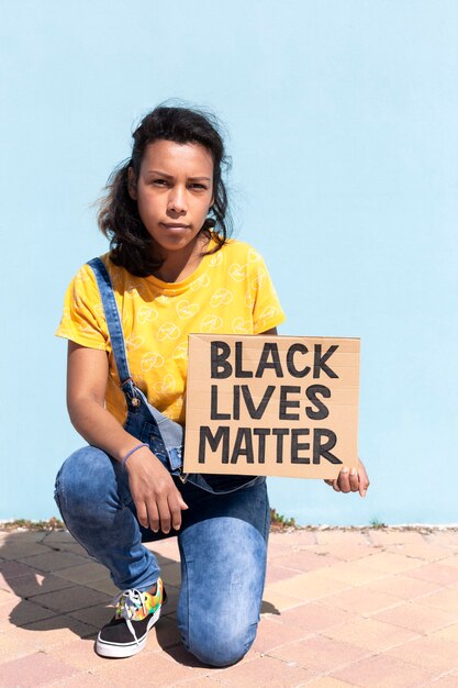 Retrato de mujer latinoamericana con actitud seria sosteniendo una pancarta con el lema Black Lives Matter