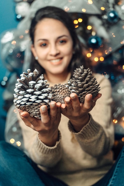 Retrato de una mujer latinoamericana sosteniendo semillas de pino decoradas con las manos detrás de un fondo navideño