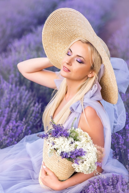 Retrato de una mujer en lavanda. Una hermosa niña está sentada sobre un fondo de flores púrpuras. Maquillaje de ojos morados.