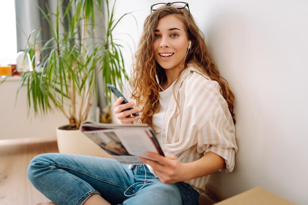 Retrato de una mujer leyendo un libro con un teléfono en las manos escuchando música a través de auriculares con cable