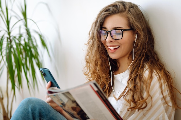 Retrato de una mujer leyendo un libro con un teléfono en las manos escuchando música a través de auriculares con cable