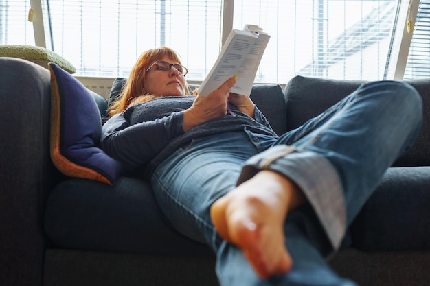 Foto retrato de una mujer leyendo un libro tendida en el sofá