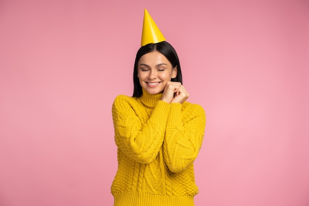 Retrato de mujer llena de alegría con sombrero cónico gracioso cogidos de la mano cerca de su rostro, sintiéndose feliz y pasando el rato en la fiesta. Celebrando el concepto de vacaciones