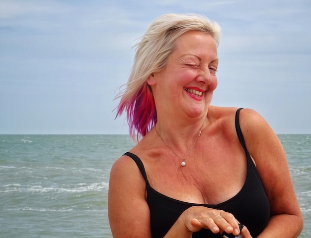 Retrato de una mujer madura alegre guiñando el ojo en la playa contra el cielo