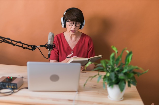 Retrato de una mujer madura con auriculares y hablando en una estación de radio en línea - podcast y concepto de transmisión