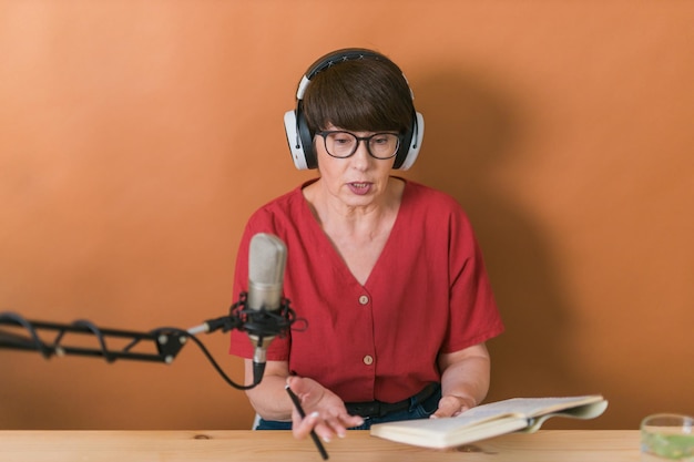 Retrato de una mujer madura que usa audífonos y habla en el podcast de la estación de radio en línea y el concepto de transmisión