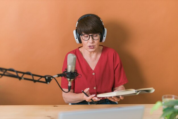 Retrato de una mujer madura que usa audífonos y habla en el podcast de la estación de radio en línea y el concepto de transmisión