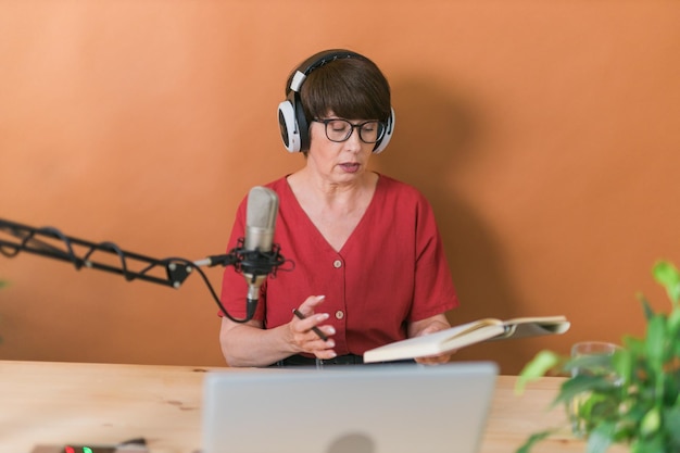 Retrato de una mujer madura que usa audífonos y habla en el podcast de la estación de radio en línea y el concepto de transmisión