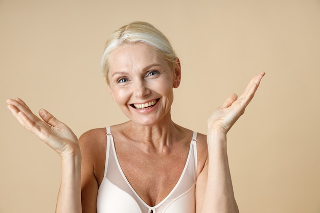 Foto retrato de mujer madura sonriente con cabello rubio en ropa interior blanca mirando a la cámara vomitando