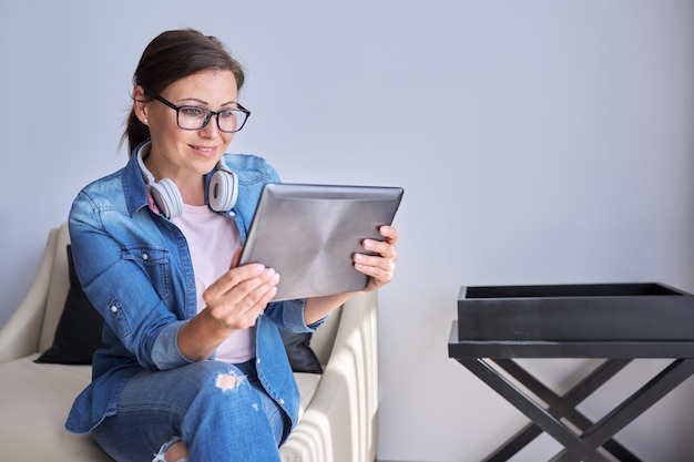 Retrato de una mujer madura sonriente mirando el monitor de una tableta digital hablando, una mujer sentada en casa se comunica en línea con amigos colegas de negocios familiares charlando, usando videollamadas, copiando espacio