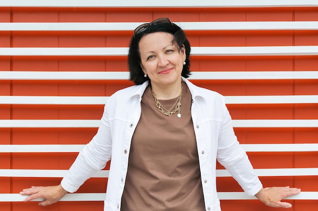 Retrato de una mujer madura sonriente en ropa de verano sobre un fondo naranja brillante con una raya blanca.