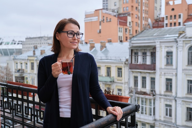 Retrato de mujer madura con una taza de té de pie en el balcón exterior