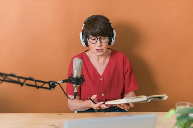 Retrato de mujer madura usando audífonos y hablando en la estación de radio en línea podcast y broadca