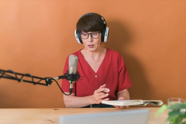 Retrato de mujer madura usando audífonos y hablando en la estación de radio en línea podcast y broadcas