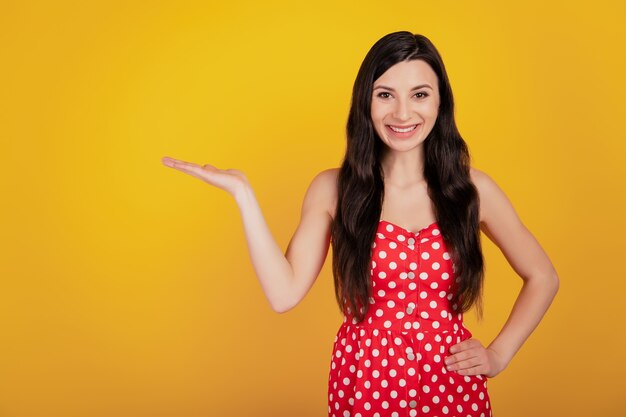 Retrato de mujer mano mantenga espacio en blanco use vestido rojo punteado sobre fondo amarillo