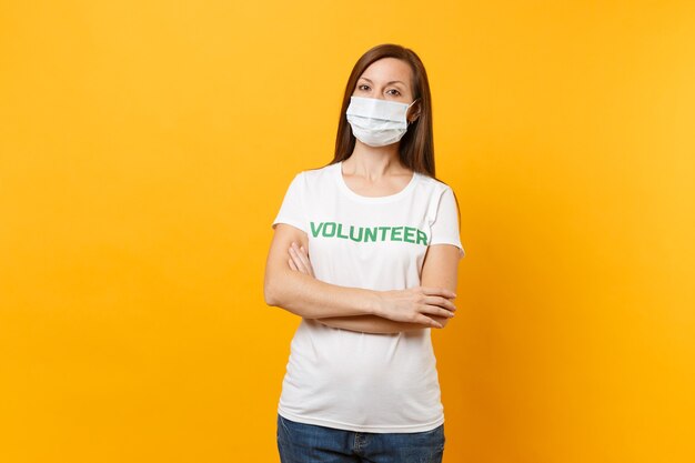 Retrato de mujer con mascarilla estéril blanca, camiseta con inscripción escrita voluntario de título verde aislado sobre fondo amarillo. Ayuda de asistencia gratuita voluntaria, concepto de salud de trabajo de gracia de caridad.