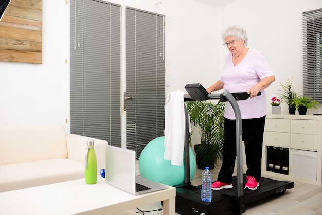 Retrato de una mujer mayor activa y dinámica haciendo deporte fitness en casa caminando en cinta