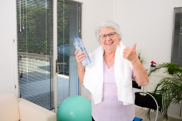 Retrato de una mujer mayor activa y dinámica haciendo deporte fitness en casa sosteniendo una botella de agua mineral