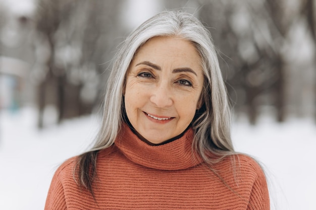 Retrato de mujer mayor con cabello gris en suéter de punto sonriendo sobre fondo de nieve en invierno