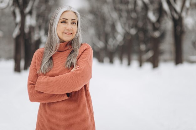 Retrato de mujer mayor con cabello gris en suéter tejido sonriendo sobre fondo en invierno