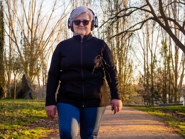 Foto retrato de una mujer mayor caminando mientras escucha música en un sendero en un parque