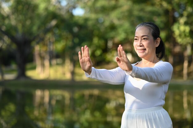 Foto retrato de una mujer mayor consciente practicando tai chi al aire libre cerca del lago en el parque de verano