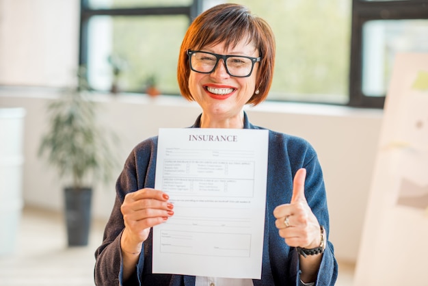 Retrato de una mujer mayor feliz con documento de seguro sentado en el interior