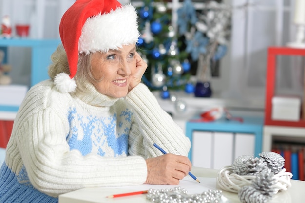 Retrato de mujer mayor con gorro de Papá Noel preparándose para Navidad escribiendo carta