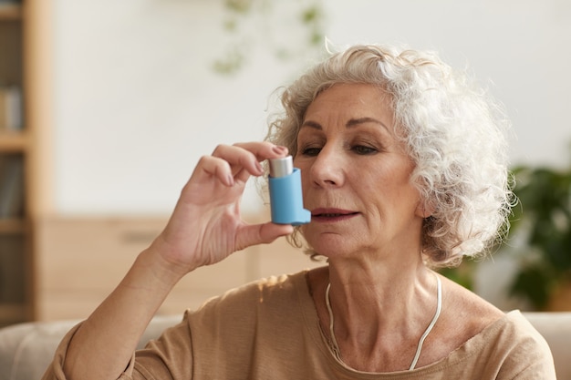 Retrato de mujer mayor con inhalador para el asma o problemas respiratorios en el hogar