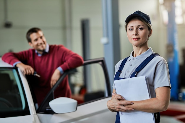 Retrato de mujer mecánica de automóviles en taller de reparación con un cliente en el fondo