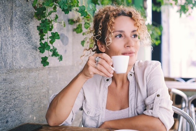 Retrato de mujer de mediana edad atractiva sonriendo y mirando mientras toma café sentado en el bar al aire libre. Mujeres adultas disfrutan bebiendo en el café durante la actividad de ocio de la tarde