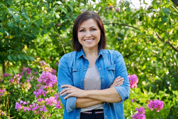 Retrato de mujer de mediana edad confiada sonriente con los brazos cruzados en el jardín