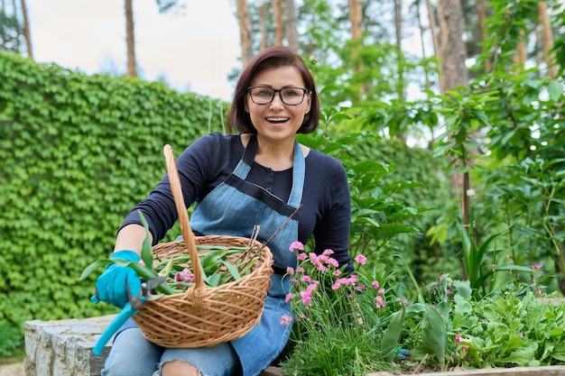 Retrato de mujer de mediana edad cuidando cama de flores en el jardín hembra está mirando a la cámara