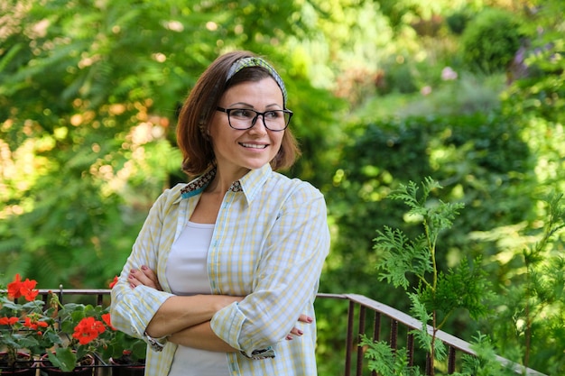 Retrato de mujer de mediana edad feliz, confiada mujer sonriente con los brazos cruzados en el balcón ajardinado al aire libre en casa