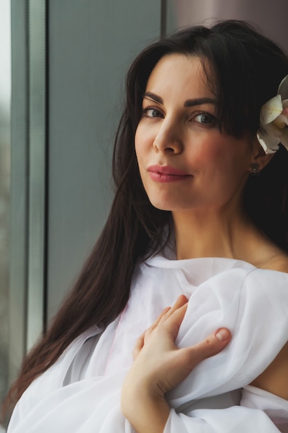 Retrato de mujer de mediana edad con flor en el cabello en la ventana de la casa