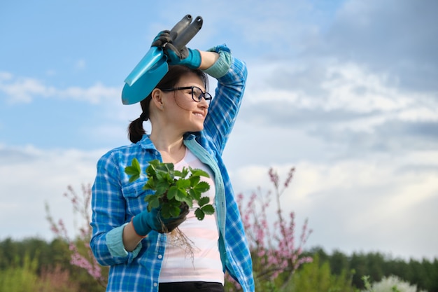 Retrato de mujer de mediana edad en jardín con herramientas, arbustos de fresa