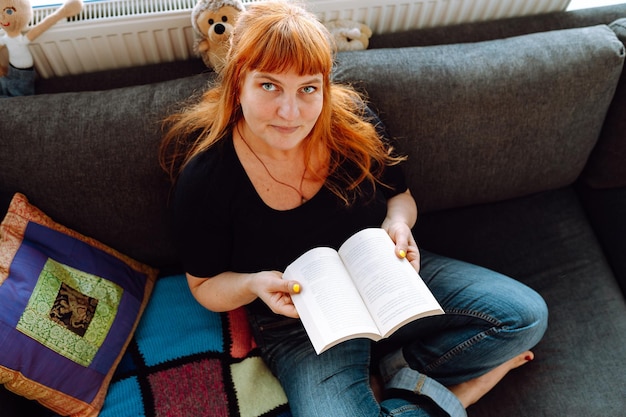 Foto retrato de una mujer de mediana edad leyendo un libro mientras está sentada en el sofá