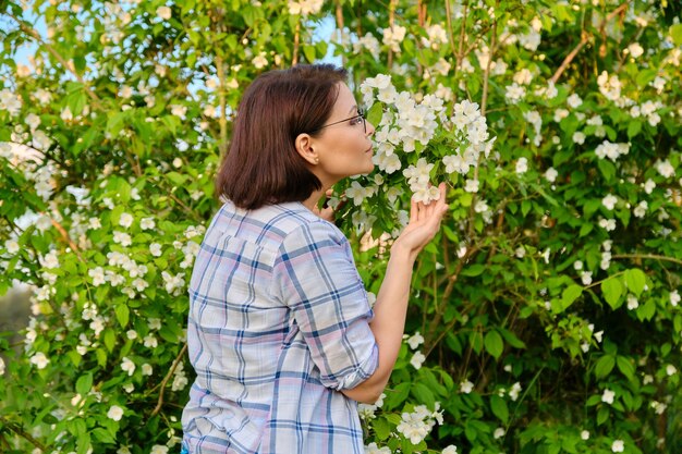 Retrato de una mujer de mediana edad sonriente cerca de un arbusto de jazmín en flor