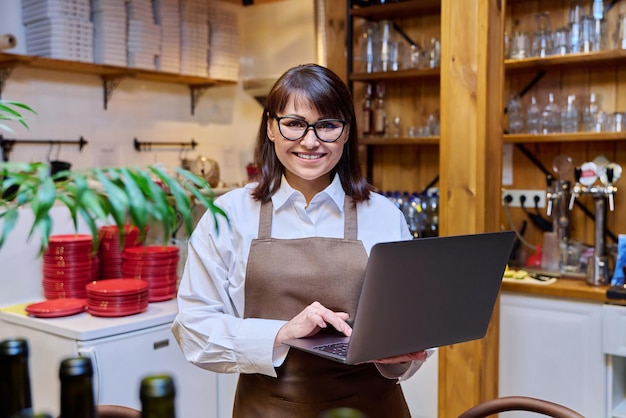Retrato de una mujer de mediana edad trabajando en un restaurante con una computadora portátil